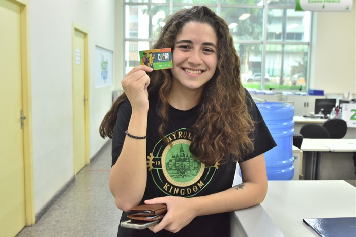 Garota branca, vestindo camiseta preta e segurando um cartão de benefício do PLE